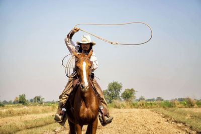 Portrait of cowboy holding rope while riding horse on land