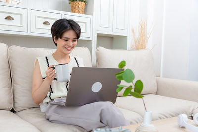 Young woman using laptop while sitting on sofa at home