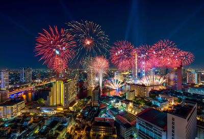 Firework display in city against sky at night