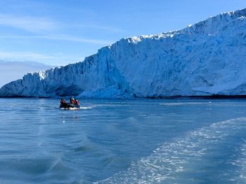 Group of people in small boat at sea against glacier in antarctica