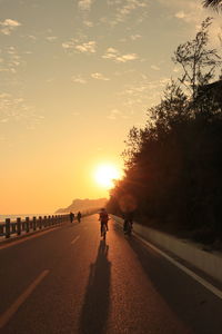 People walking on road against sky during sunset