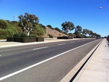 Road leading towards trees against blue sky