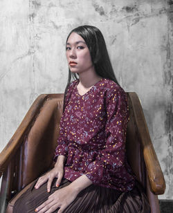 Beautiful young woman sitting against wall