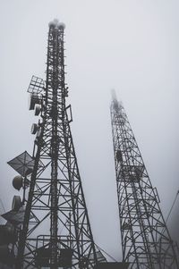 Low angle view of communications towers against sky during foggy weather