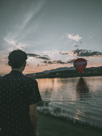 Rear view of man standing by lake during sunset