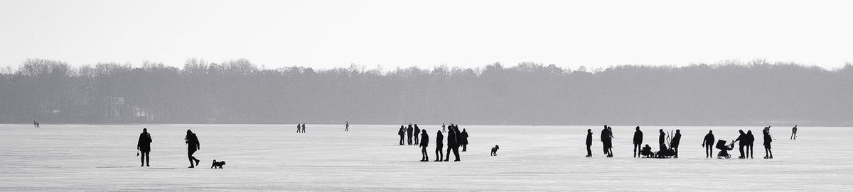 People on frozen lake against clear sky during winter