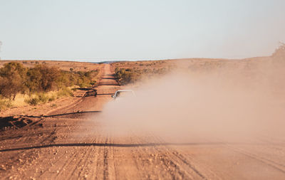Car on dirt road amidst landscape against clear sky