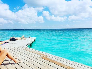 People lying on pier over sea against cloudy sky