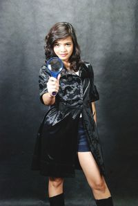 Portrait of young woman holding magnifying glass while standing against gray background