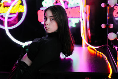 Portrait of beautiful young woman standing against illuminated lights