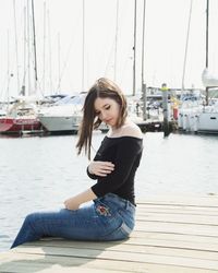 Beautiful young woman sitting on pier over sea