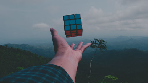 Cropped hand of woman reaching puzzle cube against sky