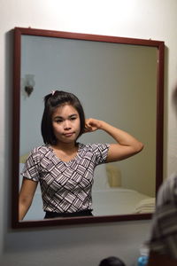 Young woman combing hair reflecting on mirror at home