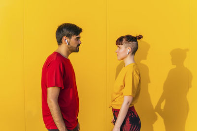 Side view of young man standing against yellow wall