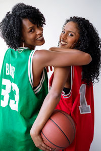 Two black women wearing basketball jerseys holding basketball on a white background