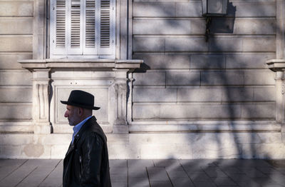 Side view of adult man in hat and leather jacket walking against wall on street. madrid, spain