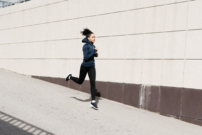 Woman jogging on footpath by wall