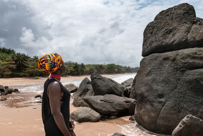 African woman standing on a beautiful beach with dark big stones