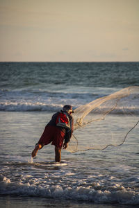 Rear view of fisherman holding fishing net at beach