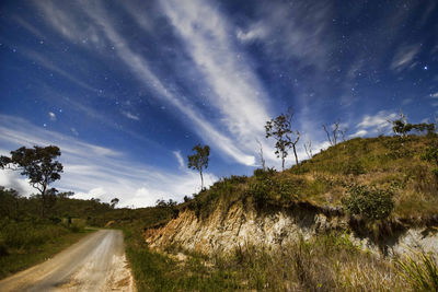 Country road amidst trees and landscape against sky