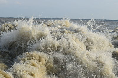 Waves splashing on shore against sky