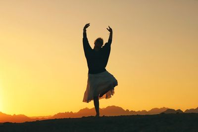 Rear view of silhouette woman standing against sky during sunset