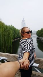 Woman sitting on riverbank against sky