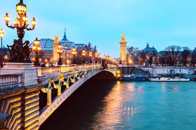 Illuminated bridge over river against sky in city