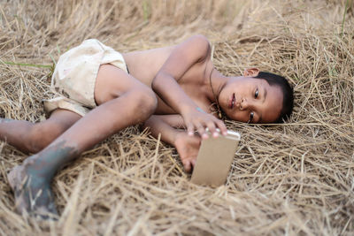 Boy using mobile phone while lying on field at farm
