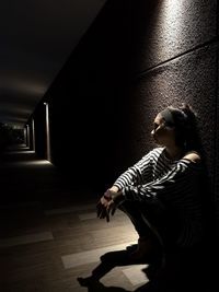 Side view of woman sitting on floor in dark corridor