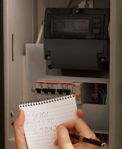 Cropped hand writing on diary against electric meter