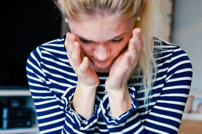 Close-up of young woman with hands on chin sitting at home