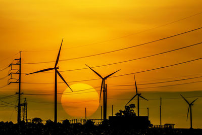 Silhouette of wind turbines against orange sky