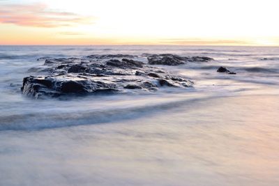 Idyllic shot of rocks in sea against sky during sunset