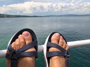 Low section of woman wearing sandal on railing against lake