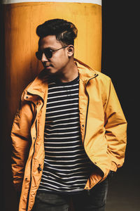 Young man wearing sunglasses standing against wall