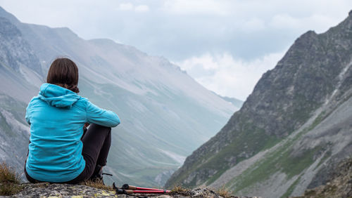 Rear view of woman sitting on rock against mountains and sky