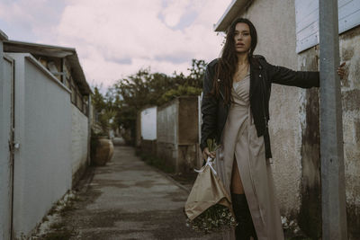 Portrait of young woman standing on footpath