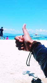 Close-up of hand holding sand at beach against blue sky