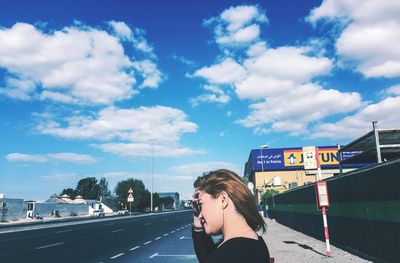 Woman with cars on road in city against cloudy sky