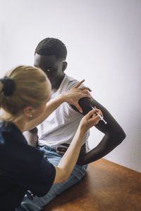 Female nurse giving vaccination on arm of male teenage patient sitting in clinic