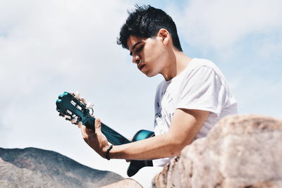 Young man photographing on rock against sky