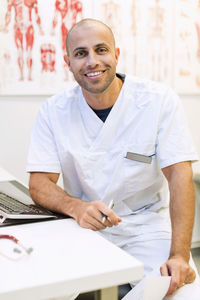 Portrait of happy male orthopedic doctor sitting at desk in clinic