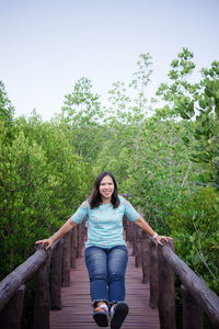 Portrait of smiling woman playing on footbridge against trees