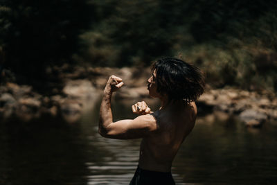 Side view of shirtless man standing by lake