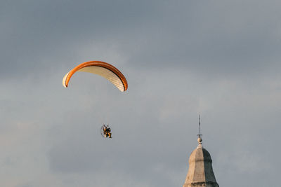 Person paragliding by building against cloudy sky