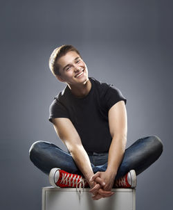 Portrait of smiling young man sitting against gray background