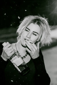 Close-up of young woman smoking cigarette while holding alcohol bottle at night