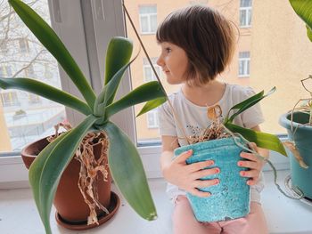 A cute girl with bob hair cut sitting at the window between house plants
