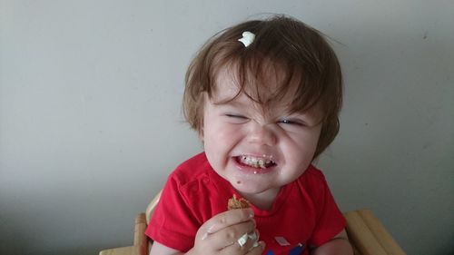 Close-up of girl showing teeth while eating food against wall